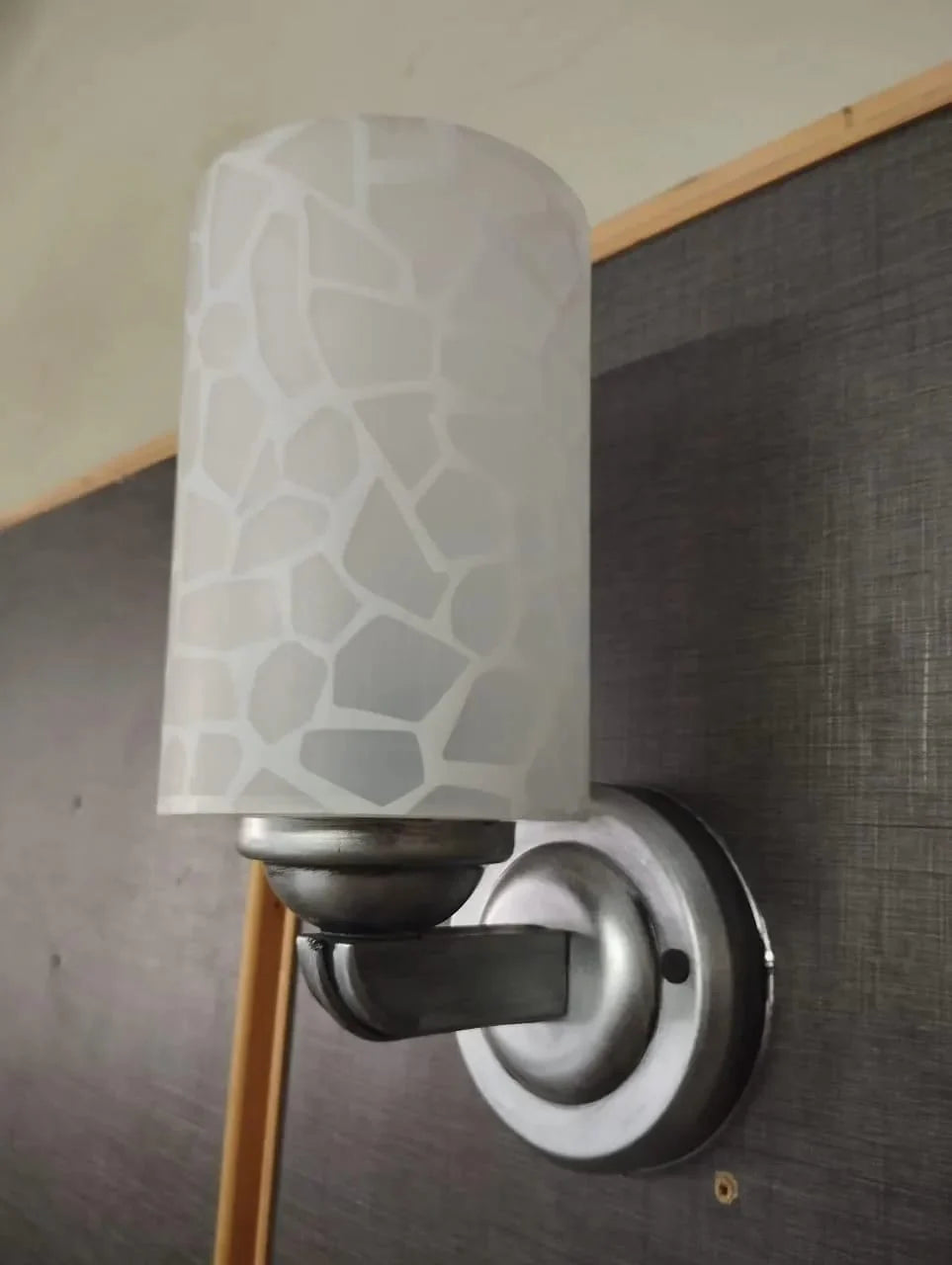 Wall-mounted light fixture with a patterned glass shade on a textured wall.
