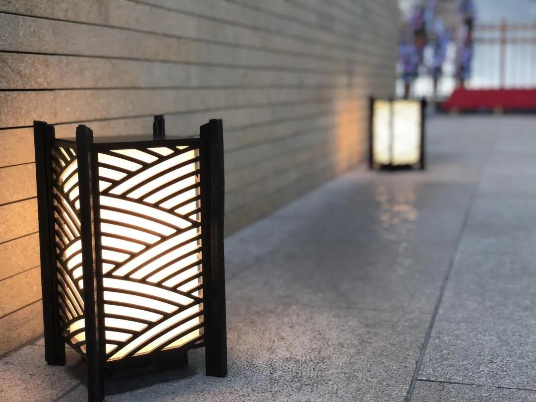 Decorative outdoor lamp with wavy pattern on a pavement next to a building.