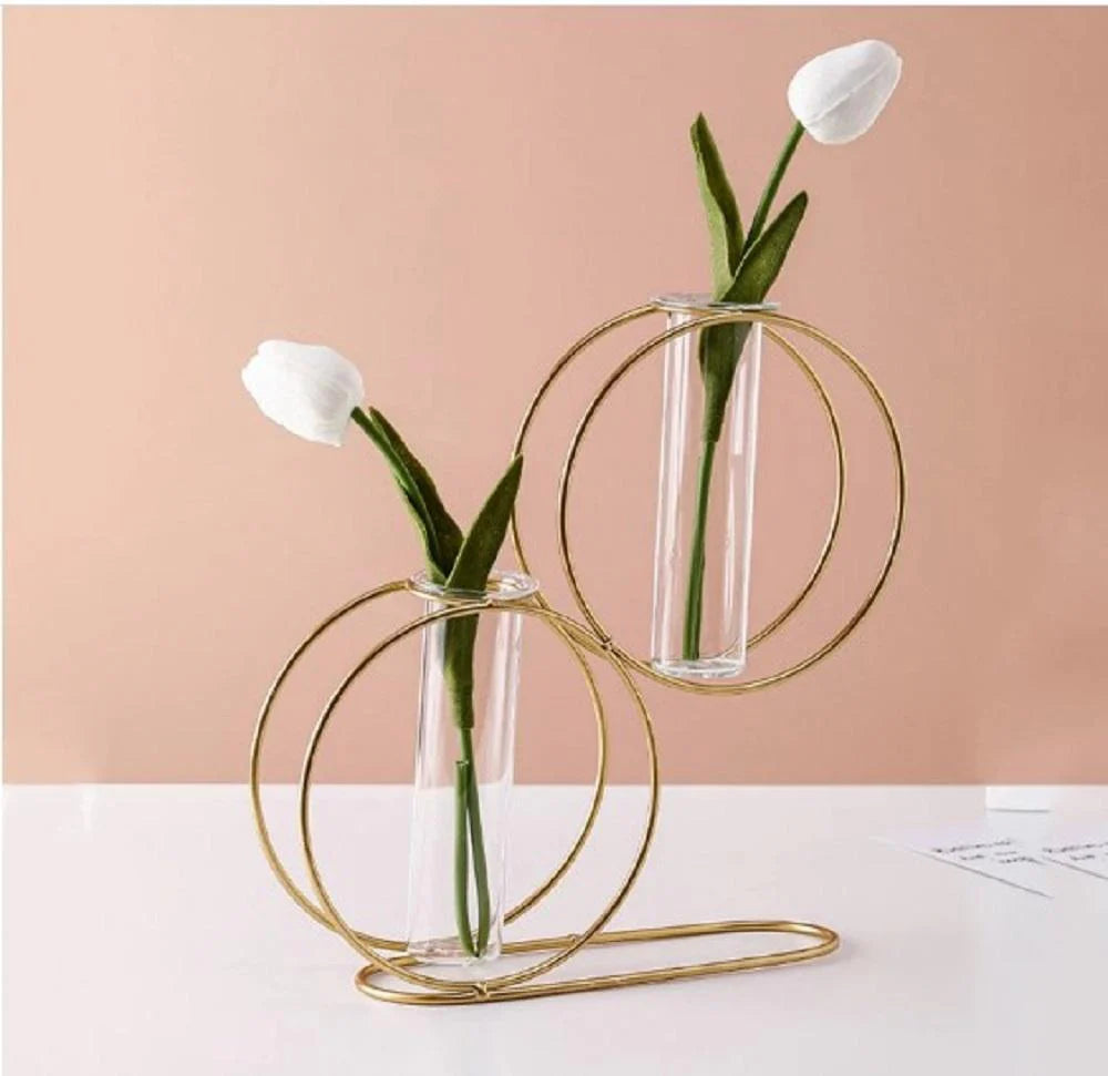 Two glass vases with gold circular designs holding white tulips on a pink background
