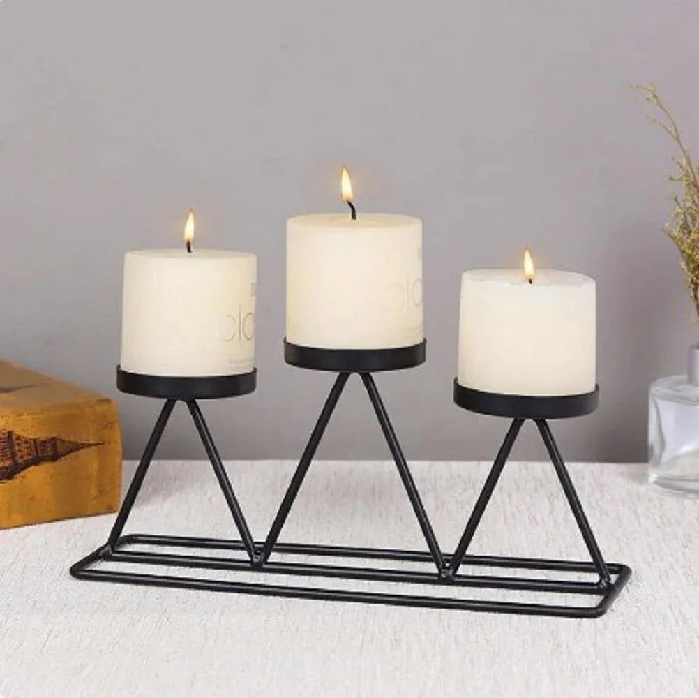 Three lit candles in black holders on a white surface with a gray background