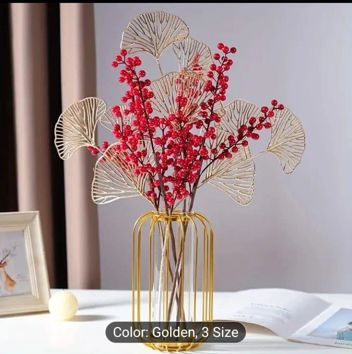 Decorative arrangement with red flowers and gold leaves in a gold vase on a table.