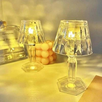 Two clear glass lamps on a surface with a blurred background