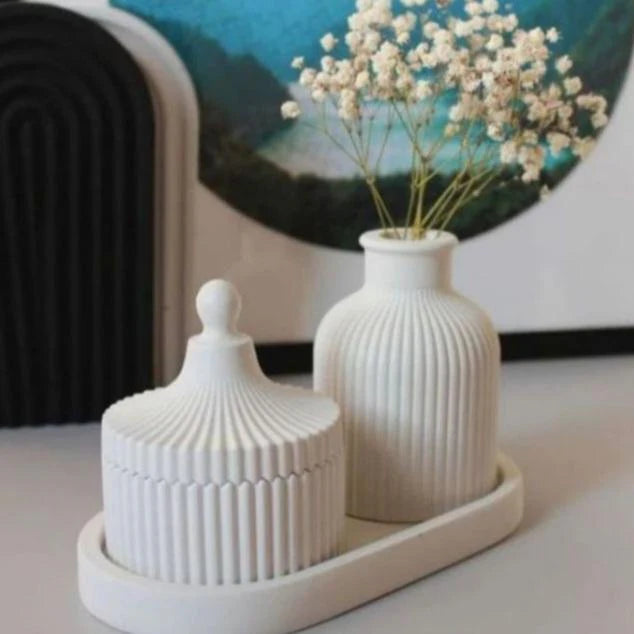 Two white ceramic containers with a small vase holding flowers on a tray.
