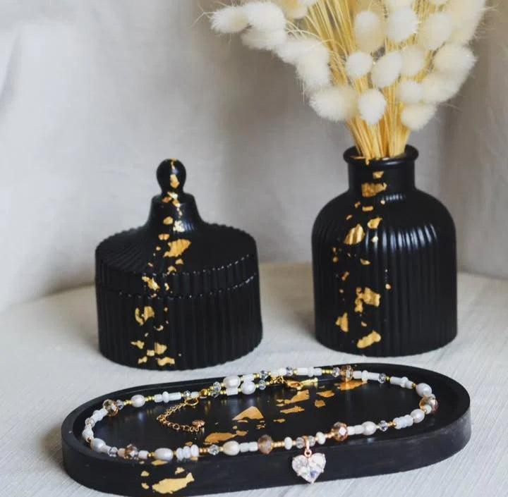 Black decorative jars with gold accents and a necklace on a black stand.