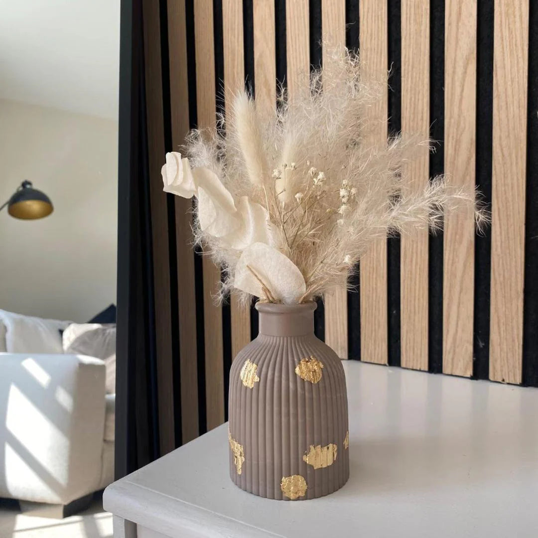 Decorative vase with dried flowers on a table in a room with striped curtains.