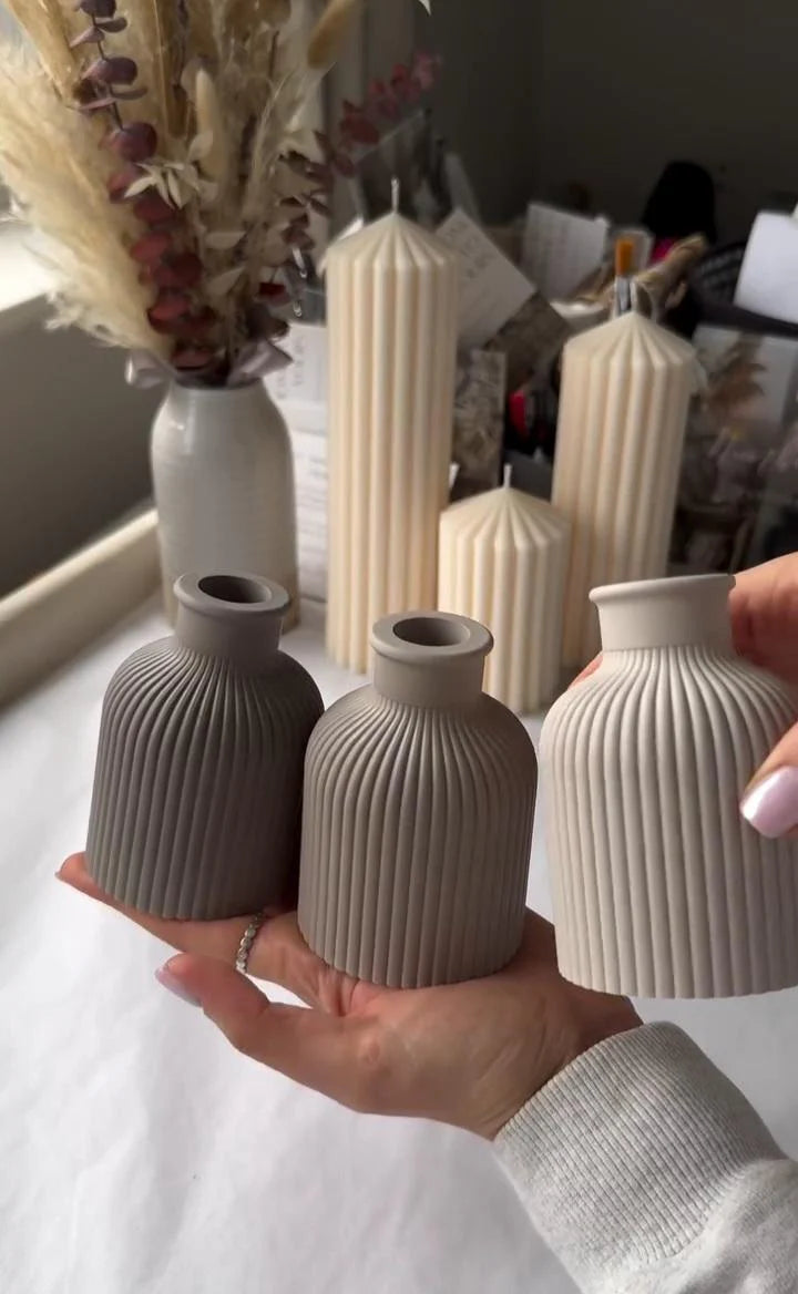 Three textured ceramic vases held by a person against a neutral background with other decorative items.