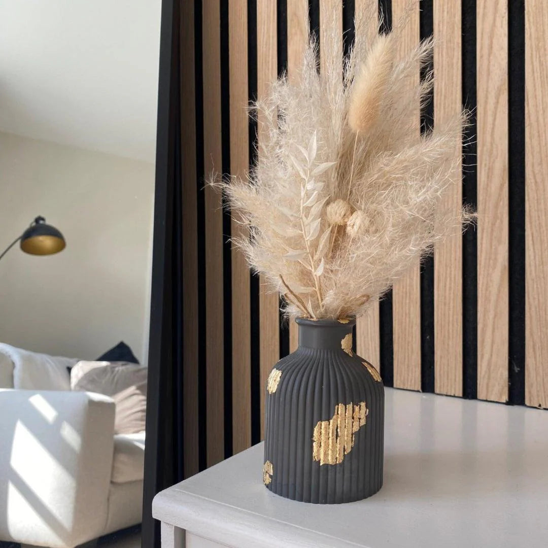 Decorative vase with dried pampas grass on a table against a striped wall.