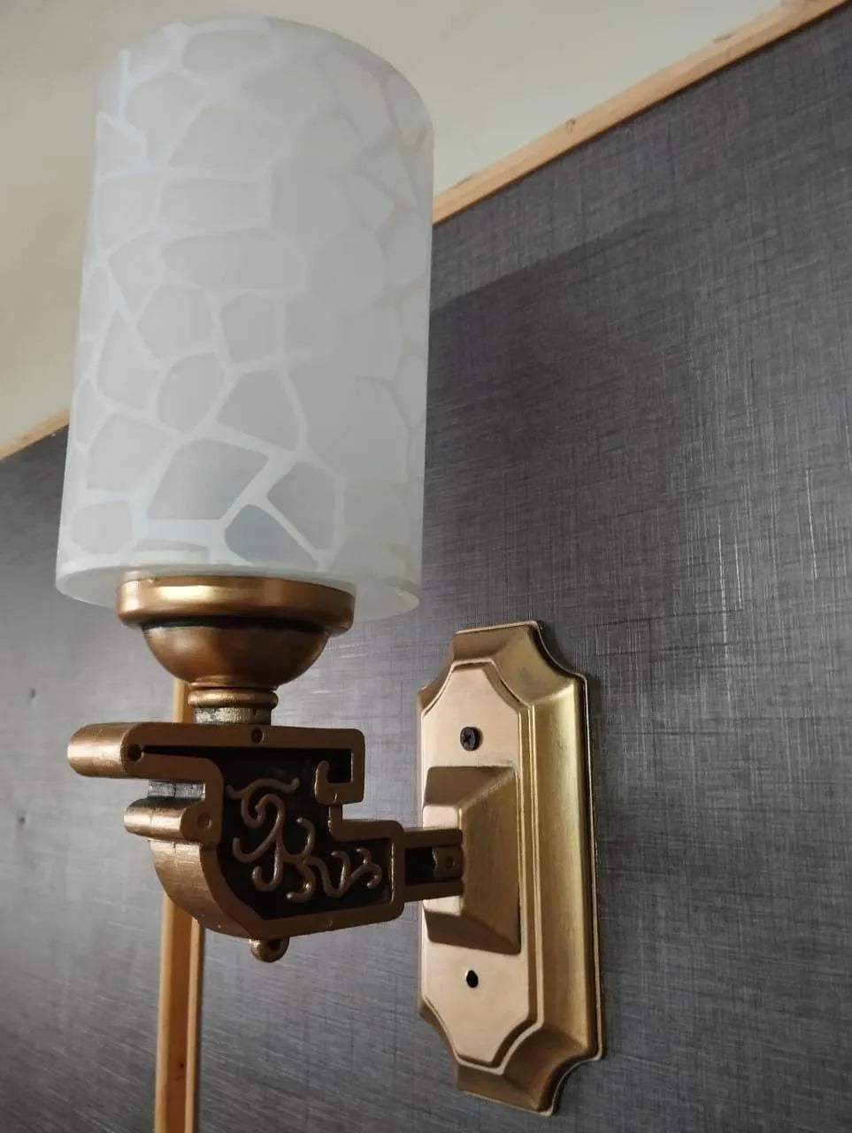 Decorative wall sconce with a textured white glass shade against a gray wall.