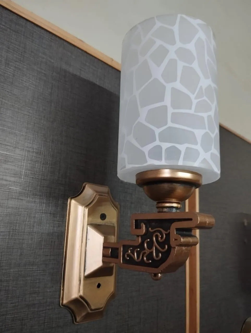 Wall-mounted light fixture with decorative lampshade on a textured wall.