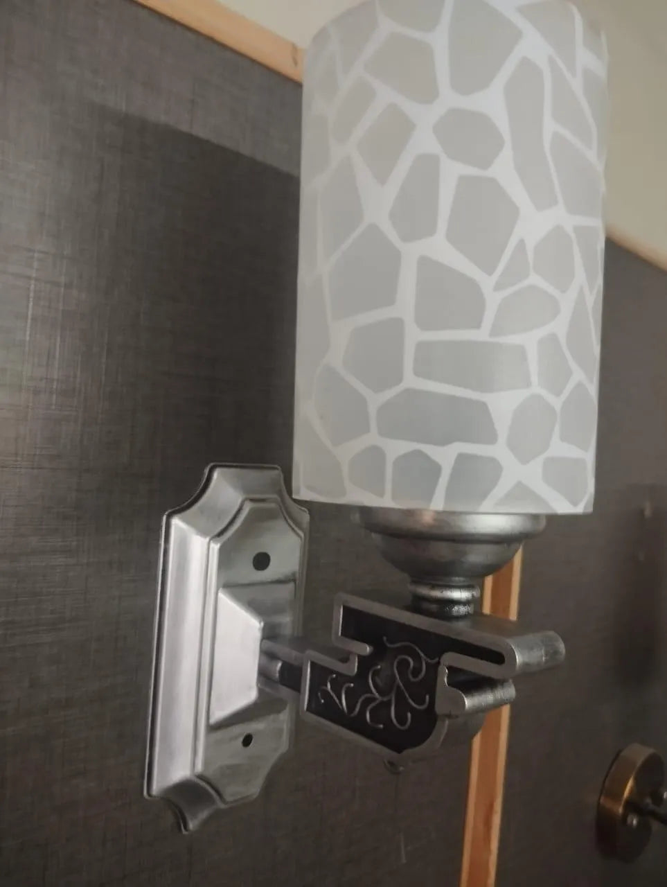 Wall sconce with a textured glass shade on a dark wall.