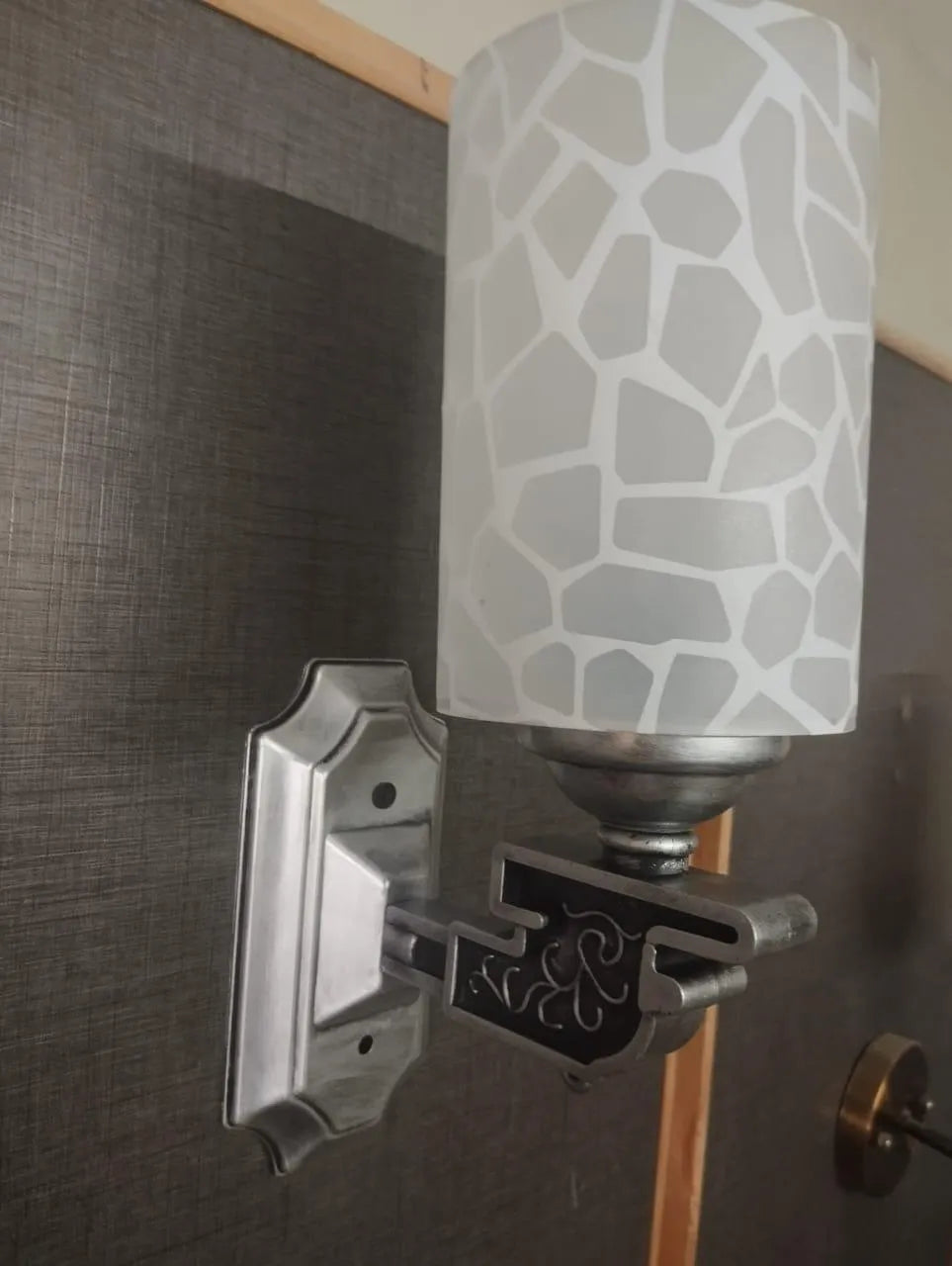 Wall-mounted light fixture with a decorative shade on a dark wall.