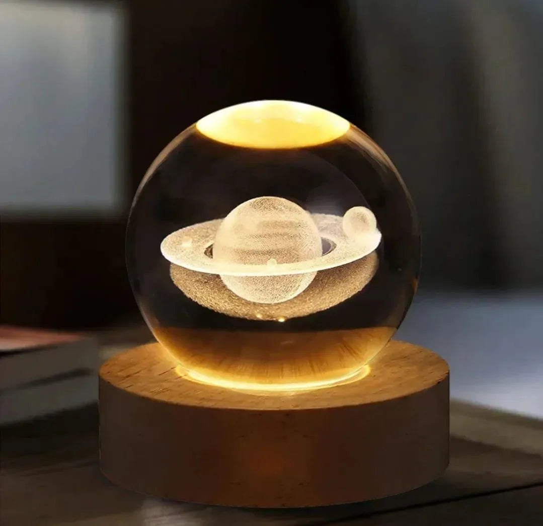 Glass sphere with Saturn model on a wooden base against a blurred background