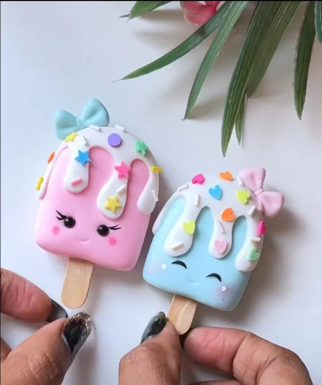 Two colorful ice cream popsicle-shaped cookies held by a person's hands on a white background with green leaves.