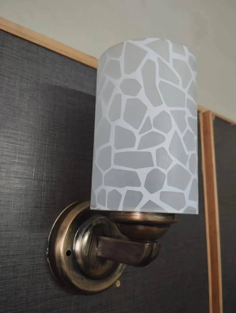 Wall sconce with a patterned white shade on a dark surface